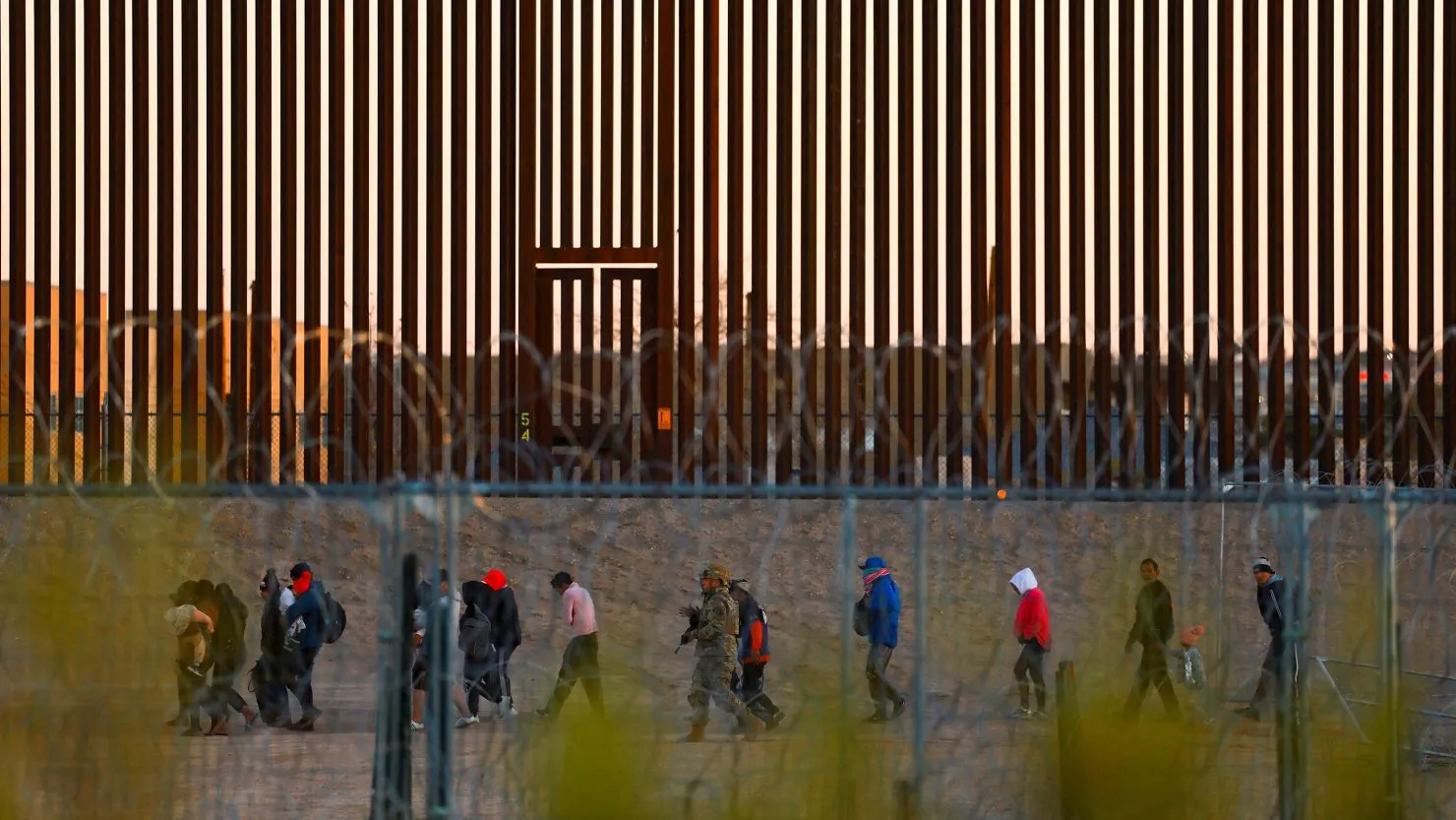 Migrants seeking asylum in the United States gather near the border wall after crossing a razor wire fence deployed to inhibit their crossing into the United States, as a member of the Texas National Guard escorts them, as seen from Ciudad Juarez, Mexico December 19, 2024. Jose Luis Gonzalez/Reuters